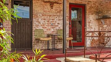 A brick building with a red door, two green chairs, a small table, and a metal railing.