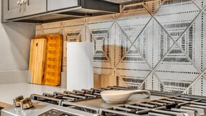 A kitchen with a modern stove, wooden cutting board, and a white paper towel holder. - Mid-Century Retreat | Private Pool+Pet Friendly (Tucson)