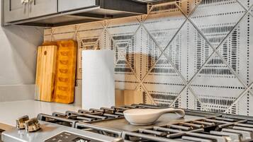 A kitchen with a modern stove, wooden cutting board, and a white paper towel holder.