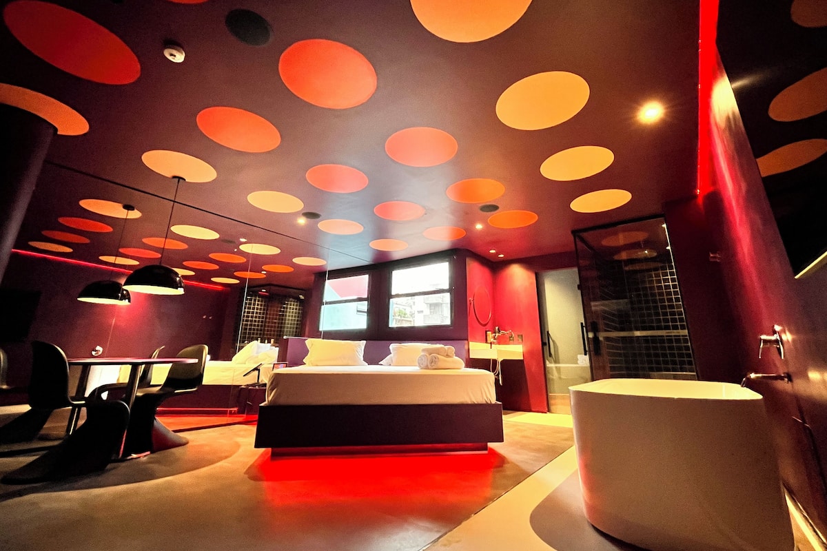 A modern bedroom with a large bed, a bedside table, and a red accent wall.