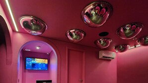 A room with pink walls, a flat-screen TV mounted on a wall, and multiple spherical mirrors on the ceiling. - Andar de Cima (São Paulo)