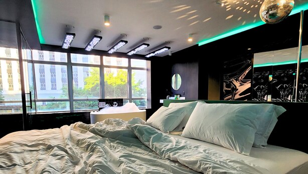 A modern bedroom with a large bed, a desk, and a window with a view of buildings and trees. - Andar de Cima (São Paulo)