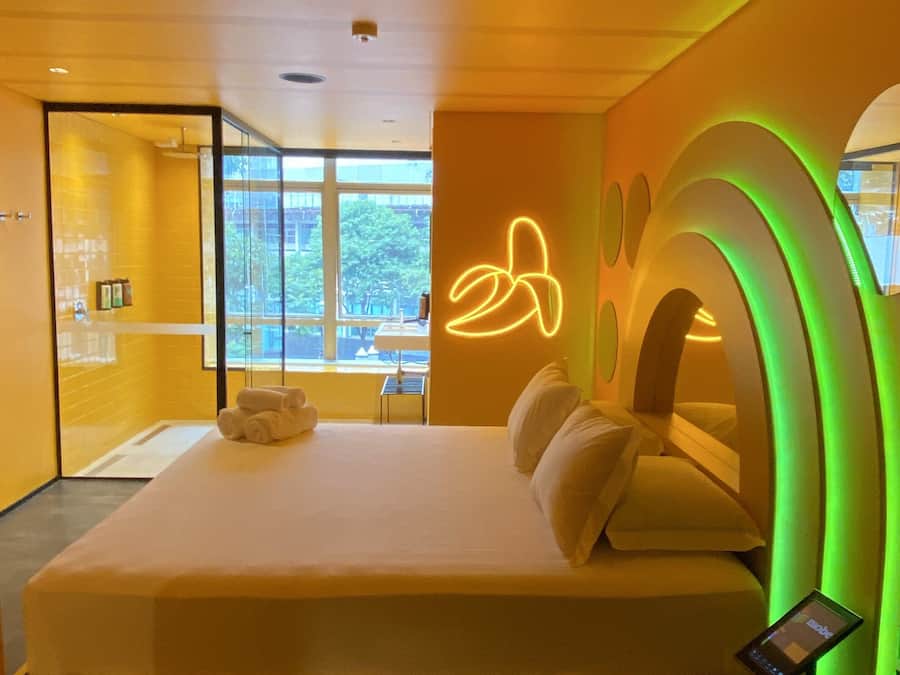 A modern hotel room with a large bed, a neon sign, and a view of the outside.