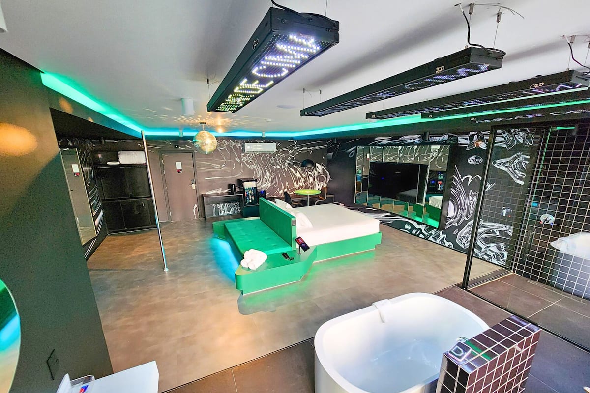 A modern hotel room with a green sofa, a white bathtub, and a large mirror.
