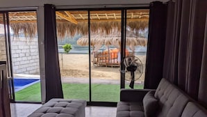 Una habitación con un gran ventanal corredera que da a una zona de piscina, un sofá gris y un ventilador.