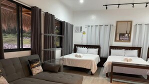 Habitación de hotel con dos camas, un sofá, un ventanal grande con cortinas, un ventilador de techo y una mesita.