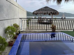 Une piscine sur le toit, bordée de carreaux bleus, entourée de plantes en pot et d’une structure à toit de chaume.