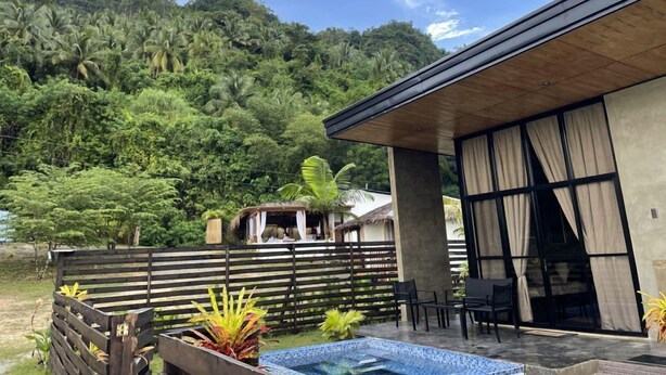 A modern building with a pool, surrounded by lush greenery and a wooden fence. - Villa Overlooking the Bay at Crystal Cove (Sipalay, Negros Occidental)