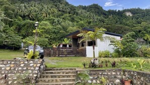 A house with a stone staircase leading to a wooden deck, surrounded by lush greenery and a forested hillside. - Villa Overlooking the Bay at Crystal Cove (Sipalay, Negros Occidental)