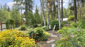 Ein Garten mit verschiedenen Pflanzen und Bäumen, einer hölzernen Pergola und einem gepflasterten Weg.