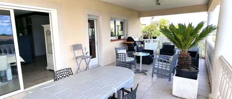 An outdoor patio area with a table and chairs, a grill, and potted plants.