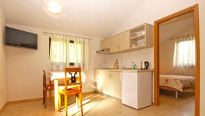 A compact kitchen with a dining area, a small refrigerator, and a bed in the adjacent room. - Apartment 1778/20511 (Istria - Kukci), 2000m from the beach (Kukci)