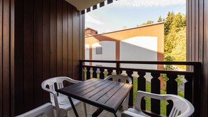 A balcony with a wooden table and two chairs, a view of a building, and a grassy area. - Apt 4 ppl near the ski runs, terrace (Morillon)