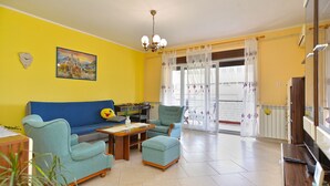 A living room with a yellow wall, a blue sofa, a green armchair, a wooden coffee table, and a television. - Apartment 2265/75351 (Istria - Pula), 500m from the beach (Pula)