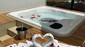 Boblebad med rosenblade og en champagneflaske på en træterrasse.