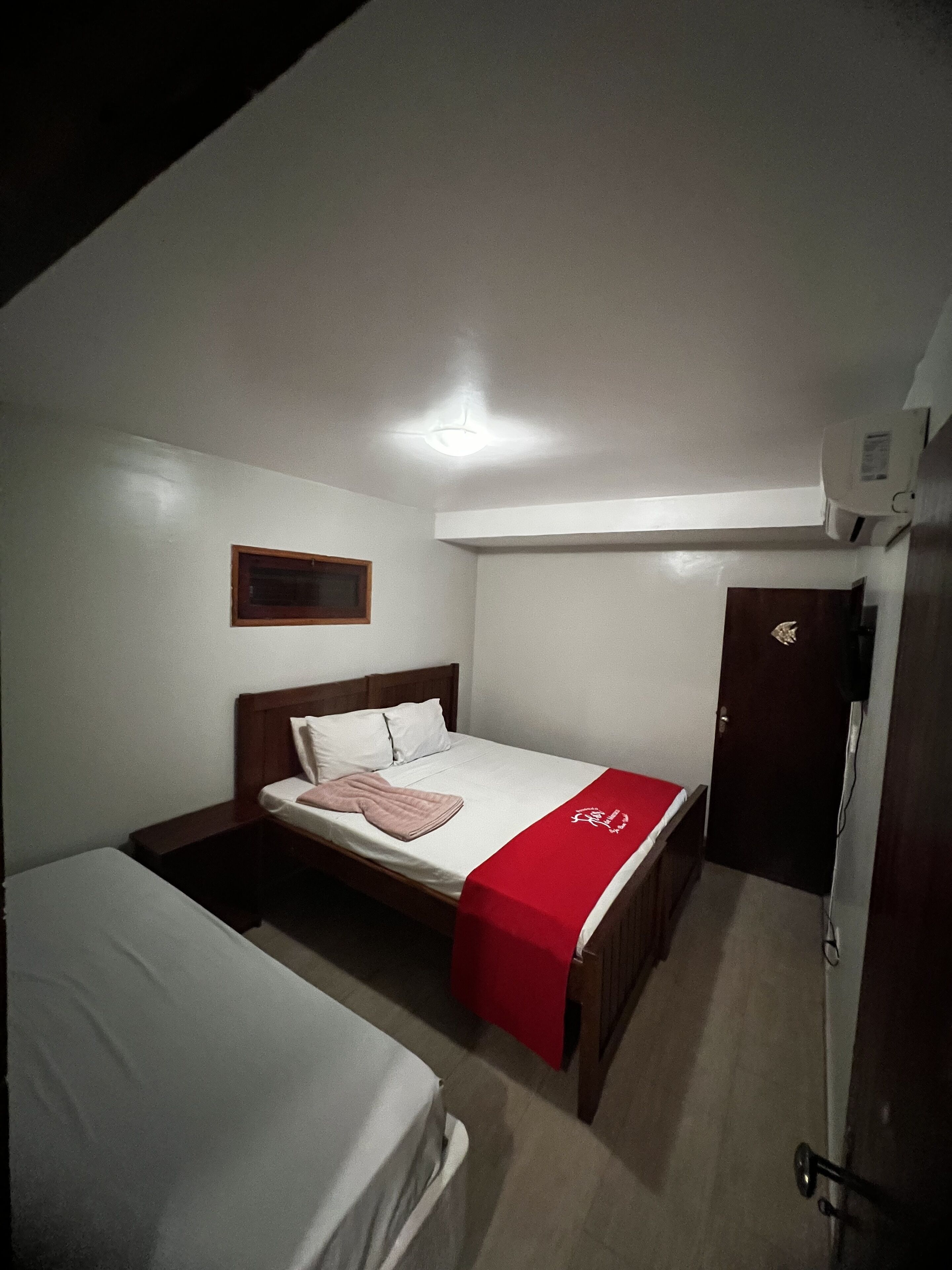 Une chambre avec un lit simple, une tête de lit en bois, une couverture rouge et un couvre-lit blanc.