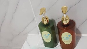 Deux bouteilles de gel douche sur une surface carrelée en marbre, avec un mouchoir en papier à proximité.
