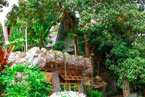 A lush indoor garden with a rock formation, wooden pergola, and various tropical plants.