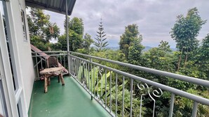 A balcony with a green floor, a wooden chair, and a metal railing overlooking a lush landscape.