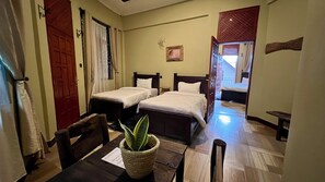 A hotel room with two beds, a dining table with chairs, a potted plant, and a view of the outside.