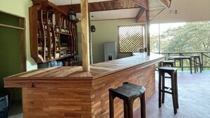 A wooden bar area with stools, a refrigerator, and shelves with bottles.