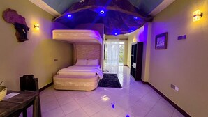 A room with a unique curved bed, a small table with a bowl, and a view of the outdoors through a door.