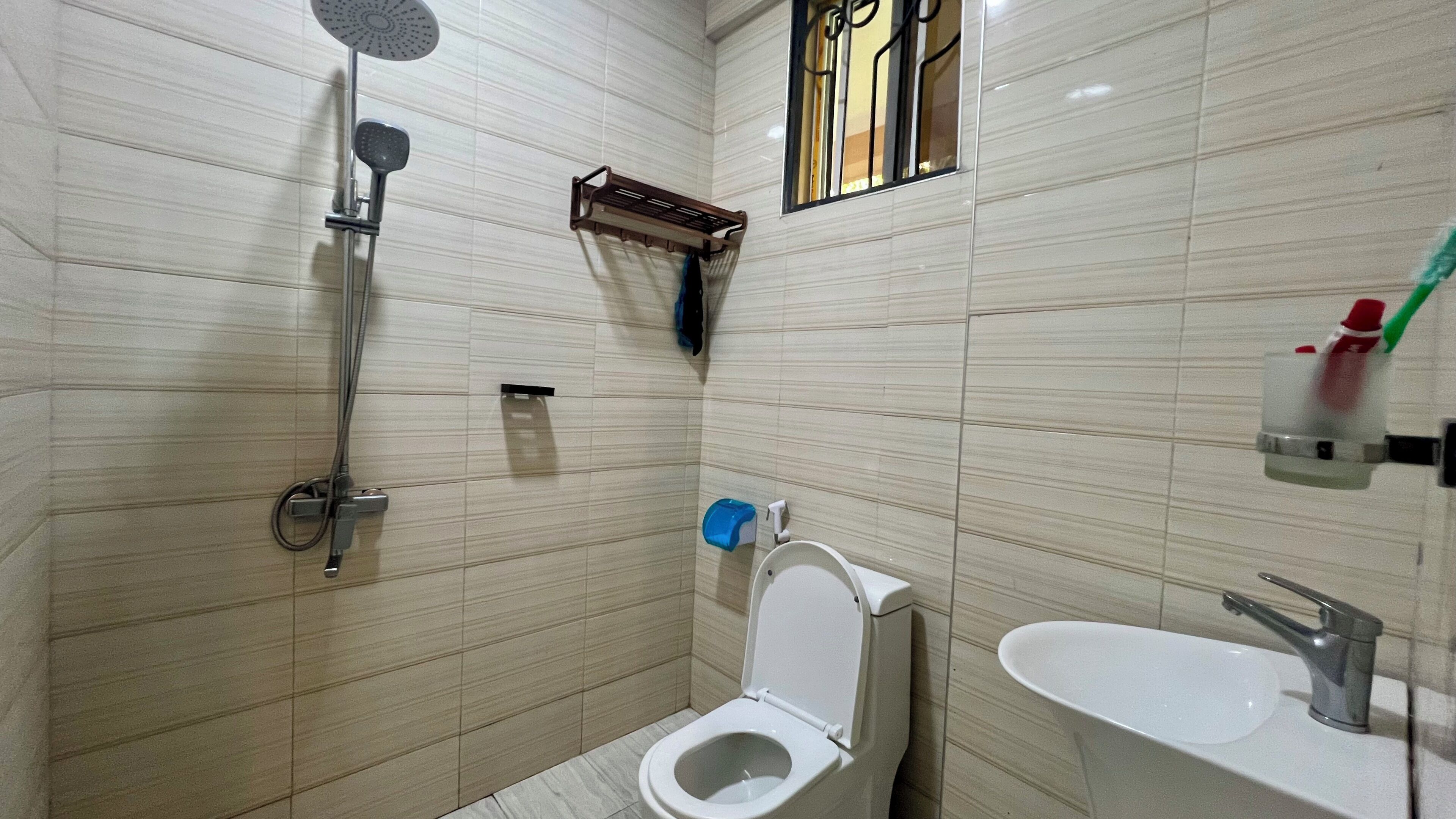 Une salle de bain équipée de toilettes, d’un lavabo, d’une douche et d’une fenêtre avec des barreaux.