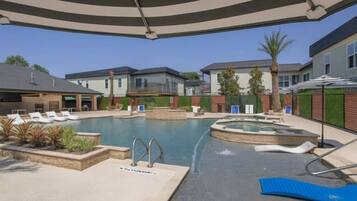 A swimming pool area with lounge chairs, a hot tub, and a covered deck.