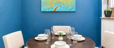 Un'area pranzo con un tavolo rotondo apparecchiato per sei persone, sedie, un vaso con una pianta e un quadro appeso al muro.
