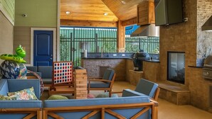 A modern kitchen with a built-in grill, a seating area with blue sofas, and a large window with a view of greenery. - Vibrant King 1BR Home near TheHeights Gym+BQQ+Pool (Houston)