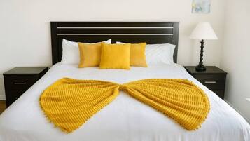 A bed with a white sheet, two yellow pillows, and a yellow blanket arranged in a bow shape.