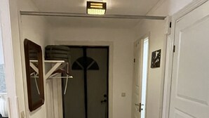 A hallway with a wooden floor, a black mat at the entrance, a white door on the right, and a door with a black and white design in the background. - Haus am See (Älmeboda)