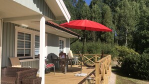 A covered outdoor area with wicker furniture and a red umbrella. - Haus am See (Älmeboda)