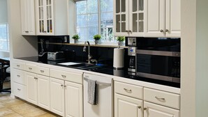 Una cocina moderna con armarios blancos, encimera negra, electrodomésticos de acero inoxidable y un ventanal que deja entrar luz natural.