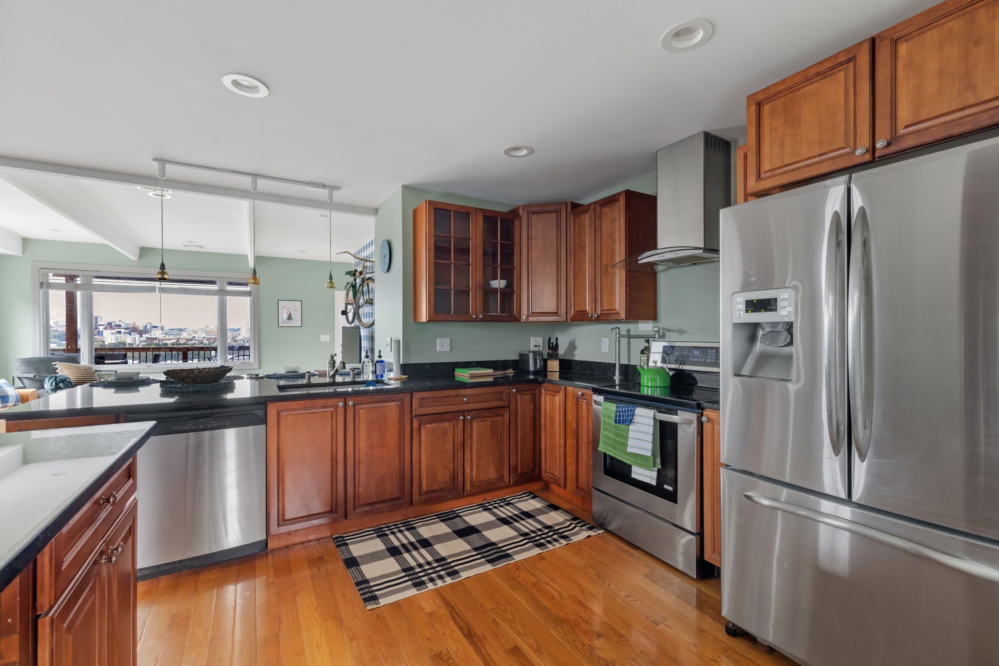 A modern kitchen with wooden cabinets, stainless steel appliances, and a large window overlooking a cityscape.