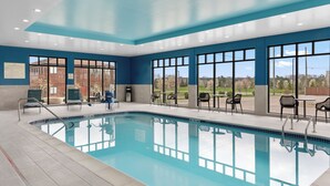 Une piscine à l’eau cristalline, entourée de grandes baies vitrées qui offrent une vue sur un paysage verdoyant.