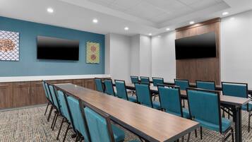 A conference room with a long table and chairs, two large flat-screen TVs mounted on the walls, and a patterned carpet.