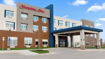 Experience the Hampton Inn's inviting entrance, featuring a blue canopy and stone pillars, surrounded by a well-manicured lawn.