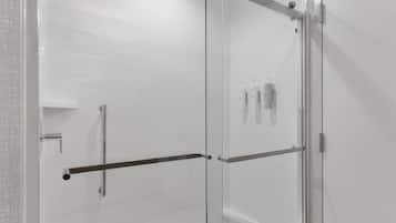 A modern shower with glass doors, a metal handrail, and a white tiled wall.