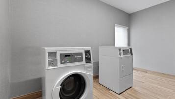 A laundry room with two front-loading washing machines and a dryer, a window, and a wooden floor.