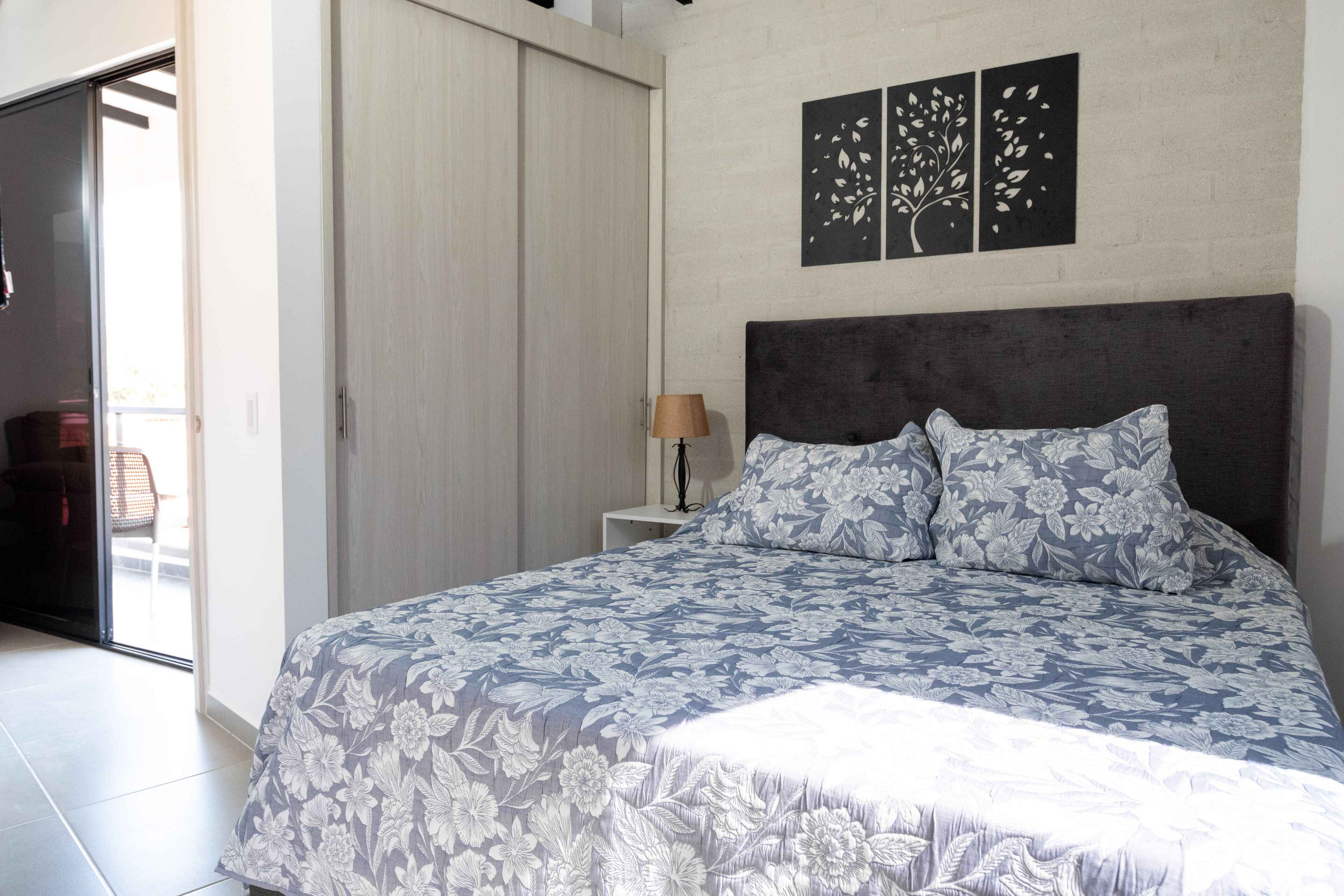 Een slaapkamer met een groot bed, een nachtkastje, een lamp en een schuifdeur naar een balkon.