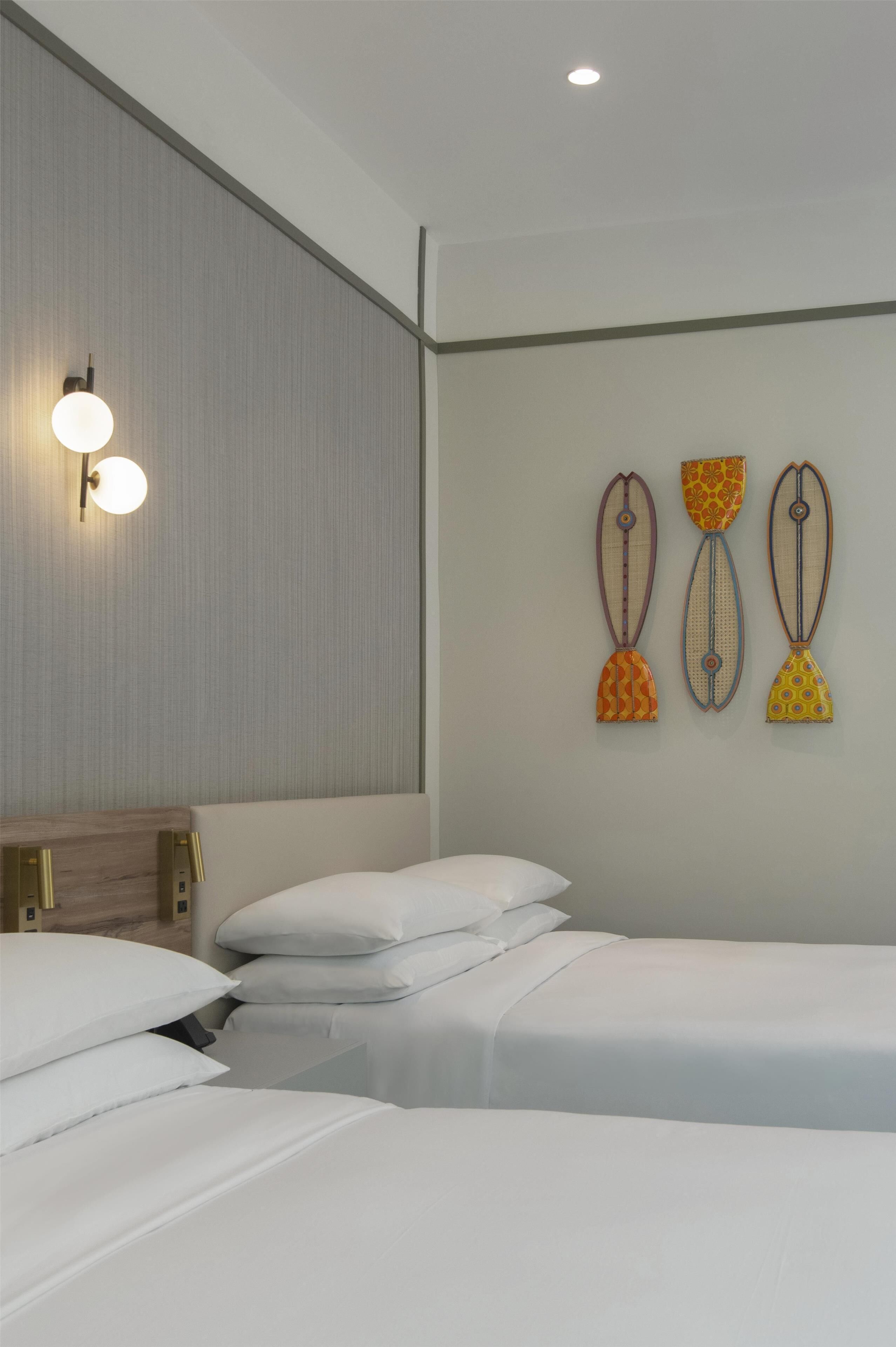 Habitación de hotel con dos camas, cabecero de madera, lámpara de pared y tres adornos colgantes.