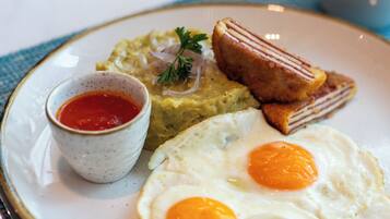 Un plato con dos huevos fritos, una rebanada de tostada, un trozo de aguacate y un tazón pequeño de kétchup.