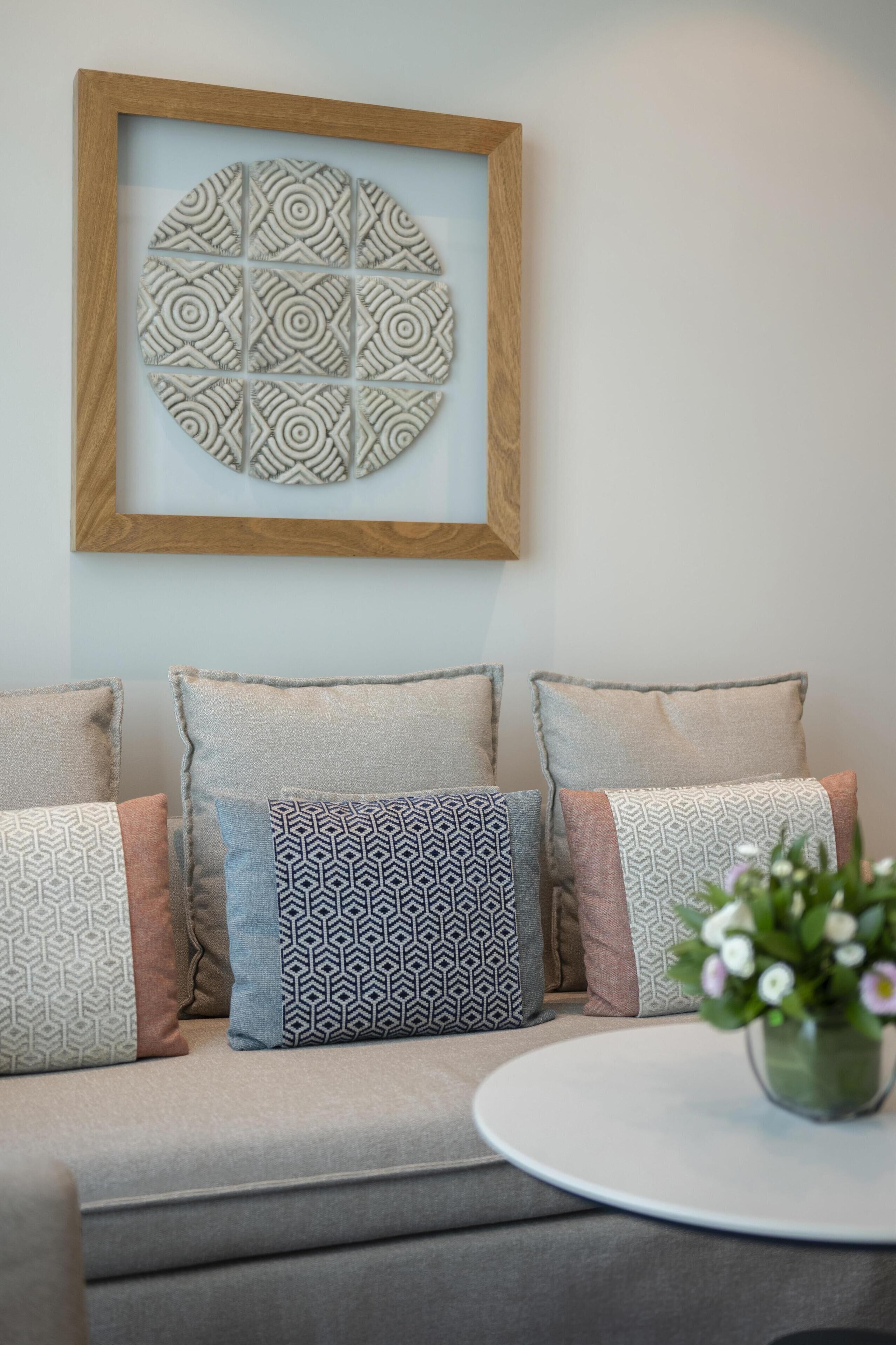 A sofa with patterned cushions, a framed artwork, and a small table with a vase.