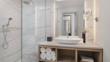 Une salle de bain moderne avec un grand miroir, un lavabo blanc et une douche dotée d’une paroi en verre.