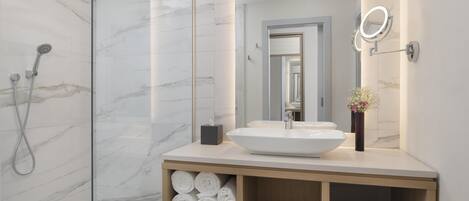A modern bathroom with a large mirror, a white sink, and a shower with a glass enclosure.
