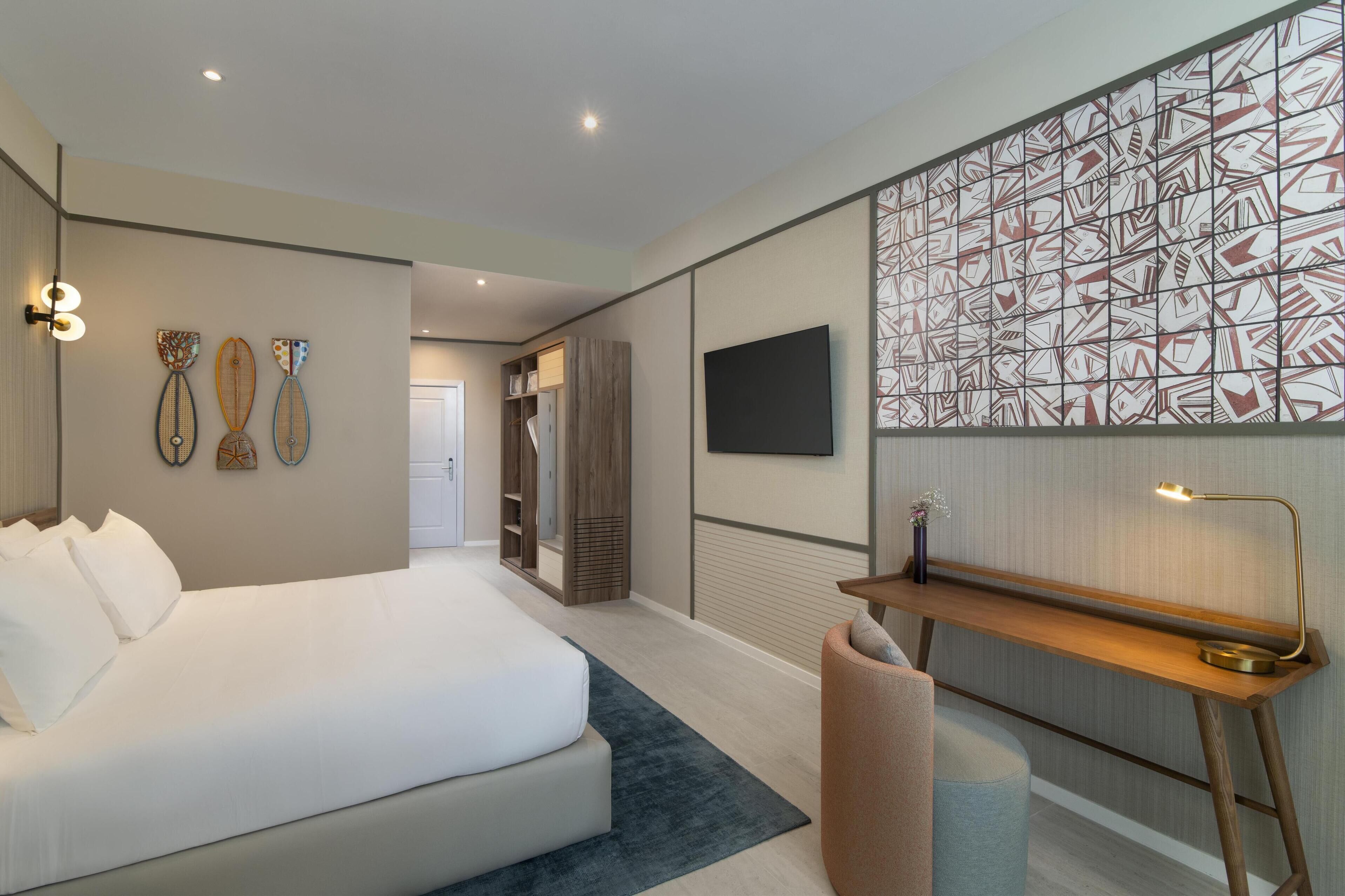 A modern hotel room with a large bed, a desk with a lamp, and a decorative wall panel.