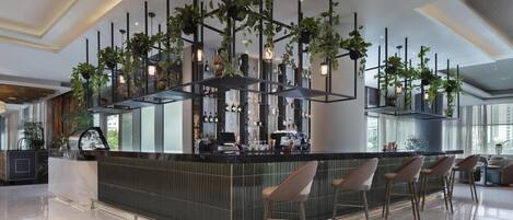 Zona de bar moderna con una isla central, taburetes y plantas colgantes.