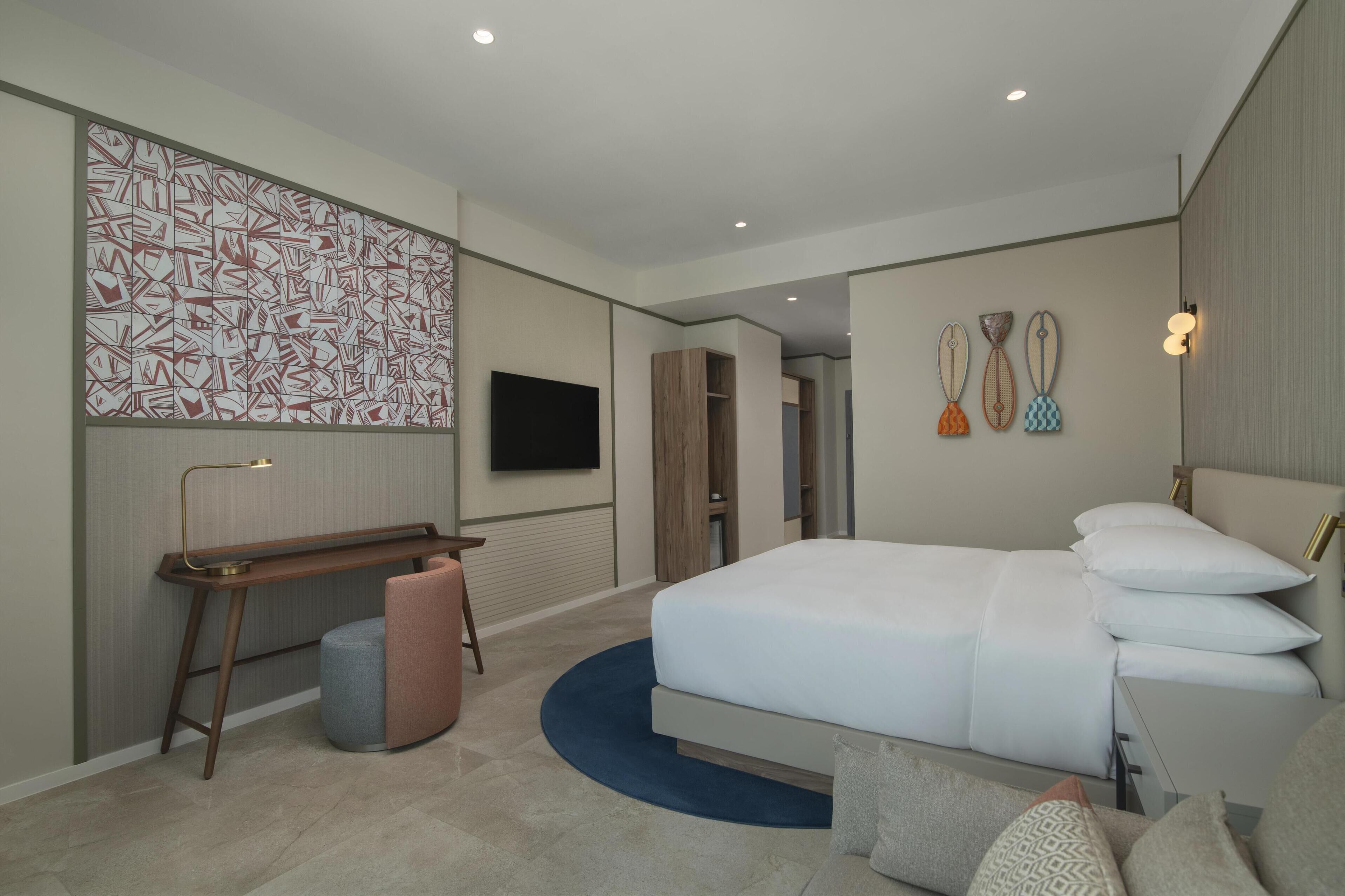 Une chambre d’hôtel moderne dotée d’un grand lit, d’un bureau, d’une chaise, d’une télévision et d’œuvres d’art décoratives au mur.