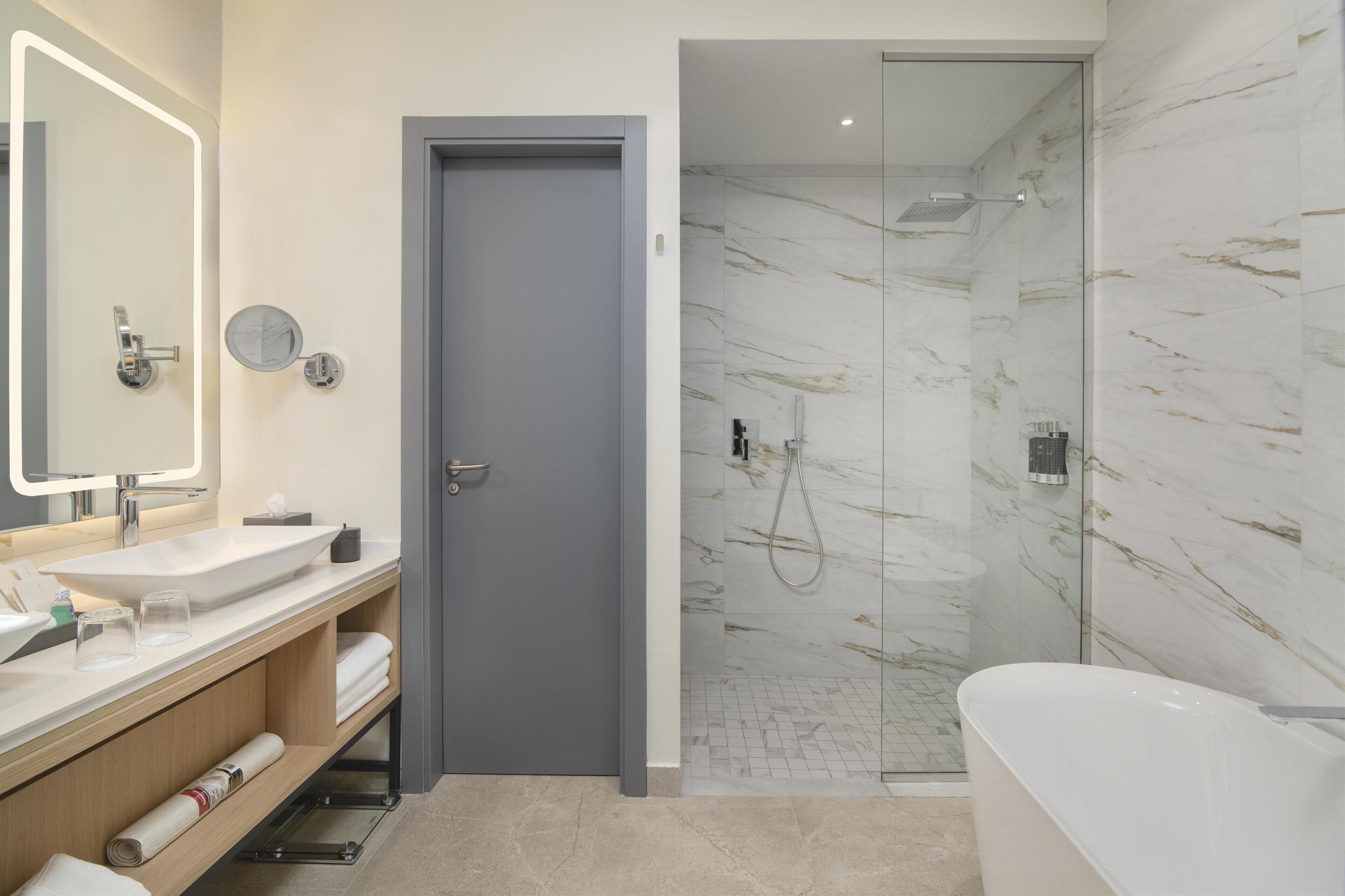 A modern bathroom with a large mirror, two sinks, a shower, and a bathtub.